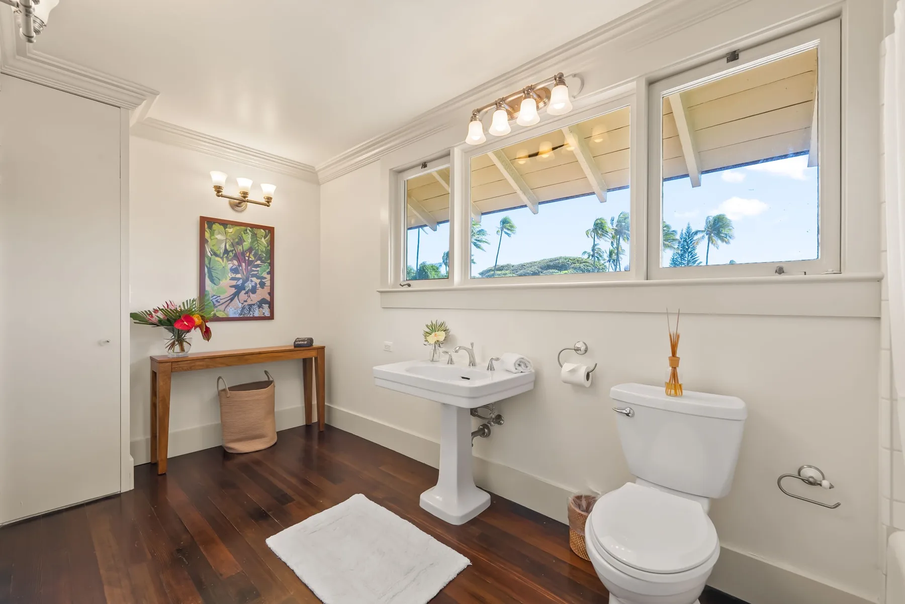 Un baño luminoso con lavabo de pedestal, inodoro y ventanas amplias.