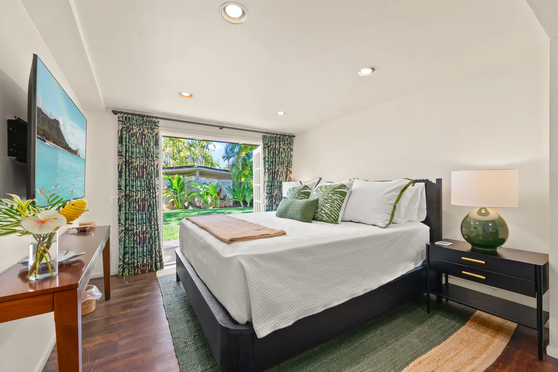 Un dormitorio luminoso con una cama tendida y puertas de cristal que dan a un jardín.