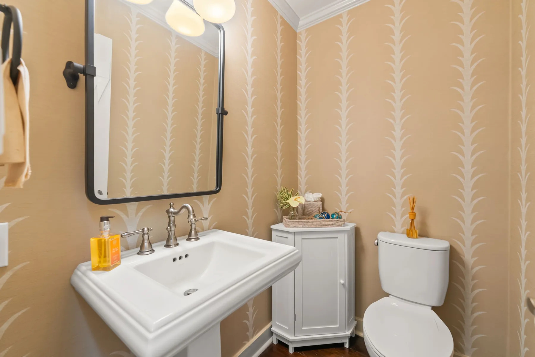 Un baño con lavabo, espejo e inodoro frente a un papel pintado estampado.