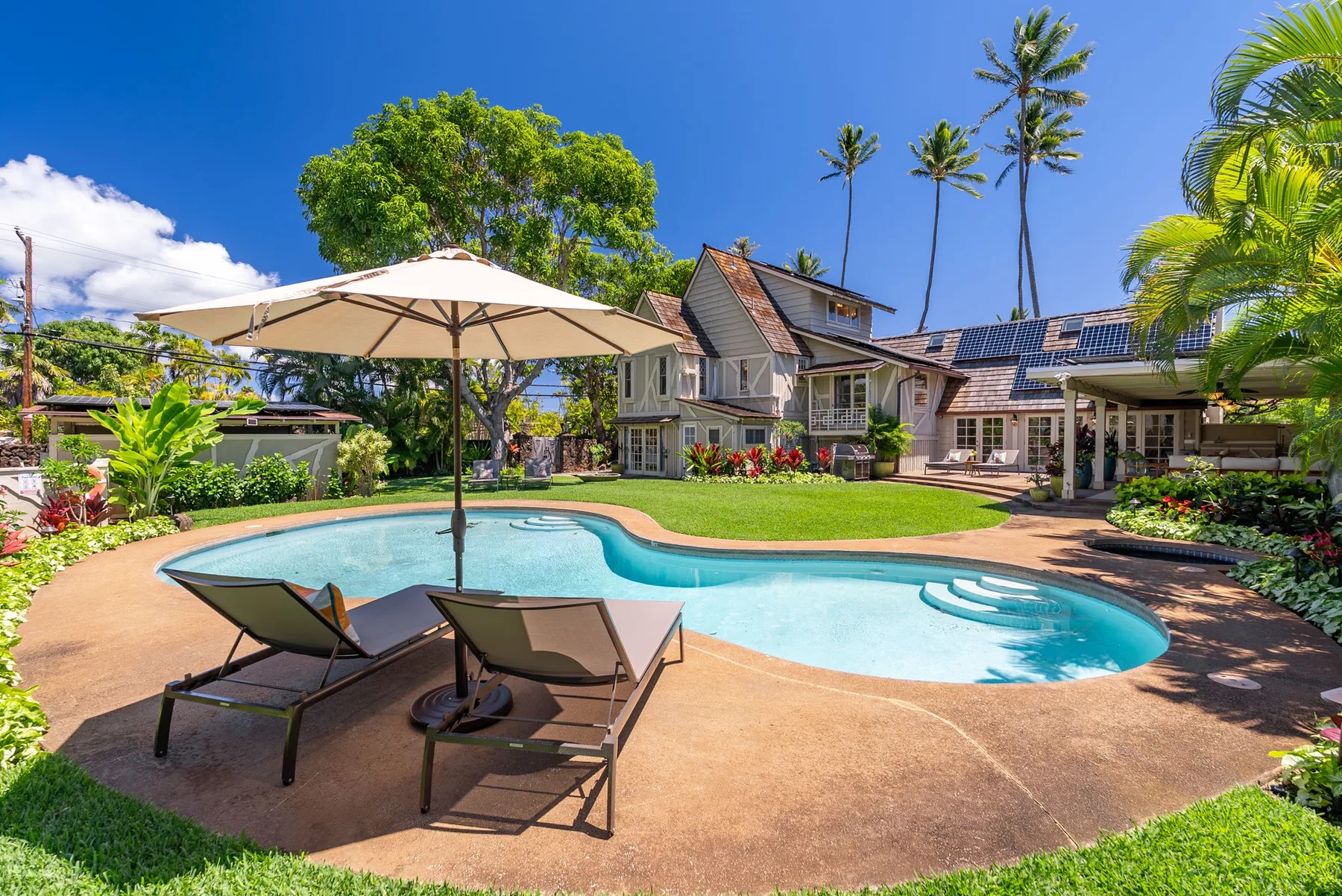 Una casa tropical está junto a una piscina curva y asientos en el patio.