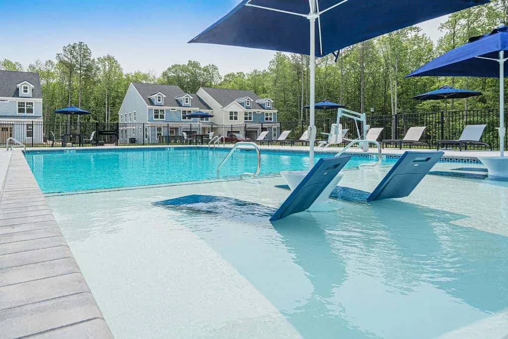 An outdoor swimming pool has shallow in-water loungers beneath blue umbrellas.