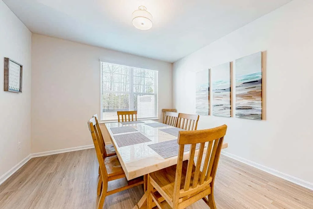 Un comedor con una mesa y sillas de madera junto a una ventana grande.