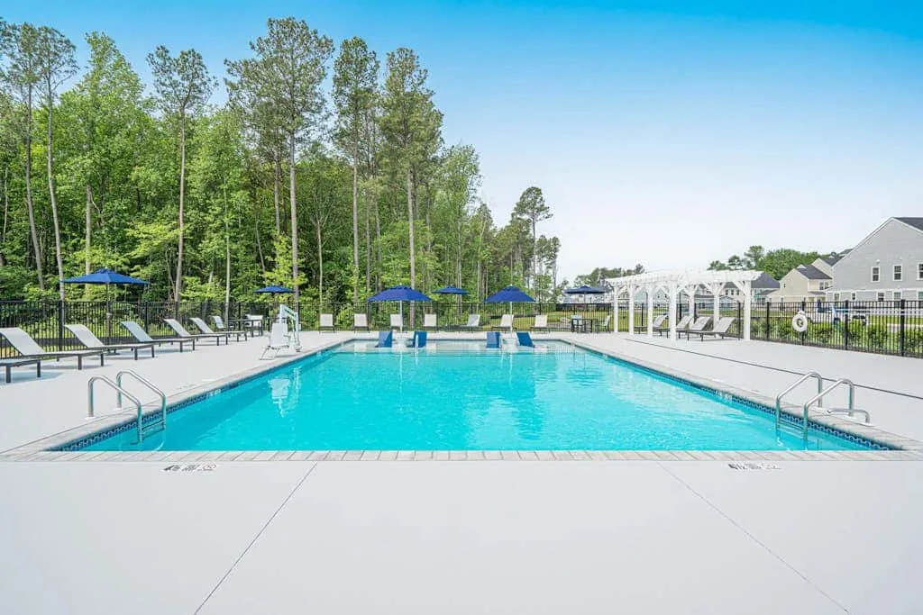 Una piscina al aire libre está rodeada de asientos reclinables y árboles altos.