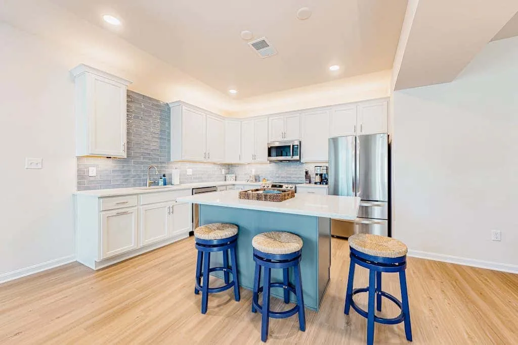 Una cocina luminosa con gabinetes blancos, electrodomésticos de acero inoxidable y una isla central.