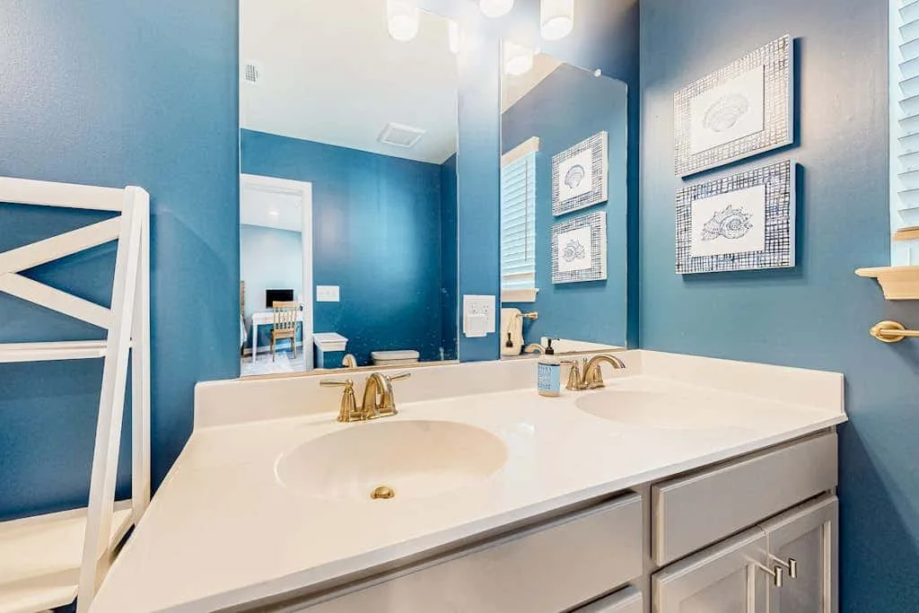 Un tocador de baño con dos lavabos y cuadros en paredes azules.