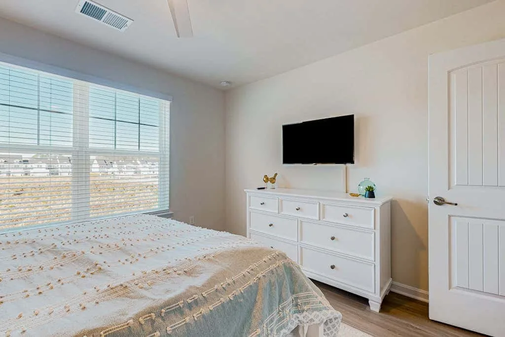 Un dormitorio con una cama junto a una cómoda y un televisor en la pared.