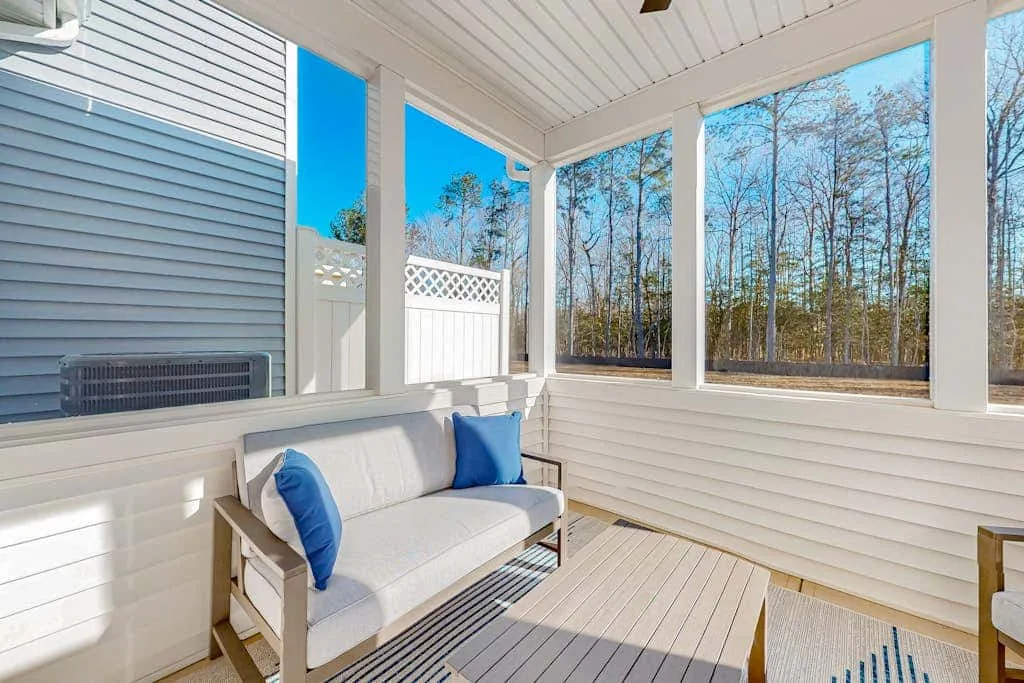 A covered porch with cushioned seating overlooking a wooded area.