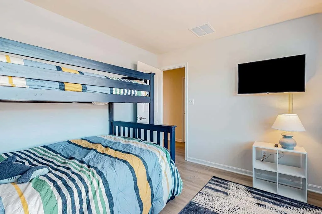 Un dormitorio con literas, ropa de cama a rayas de colores y un televisor en la pared.