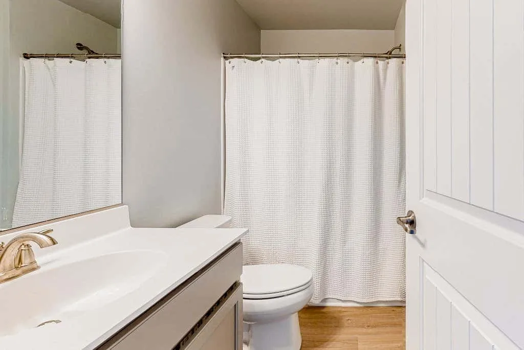 Un baño con lavabo, inodoro y cortina de ducha blanca.