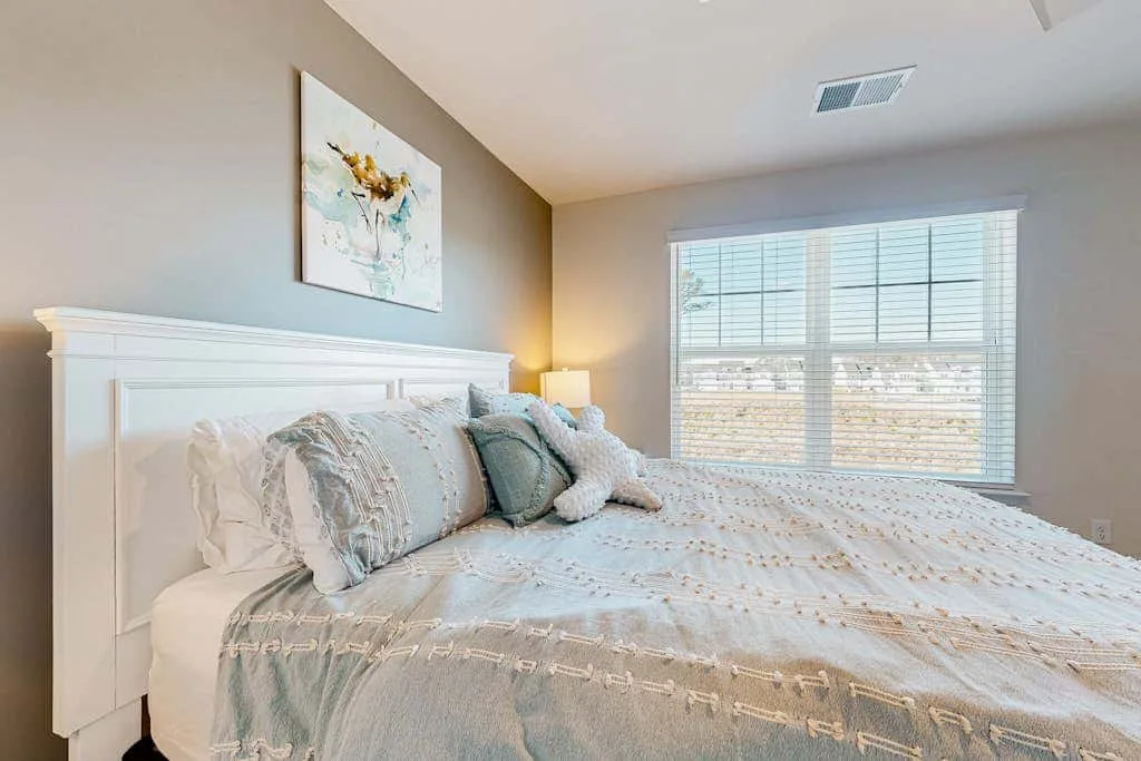 Un dormitorio luminoso con una cama tendida junto a una ventana grande.