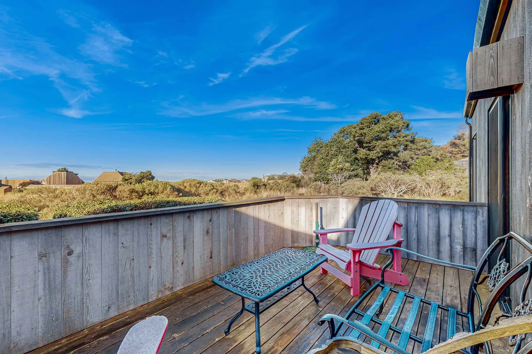 A wooden deck has colorful outdoor seating and views of the surrounding trees and sky.