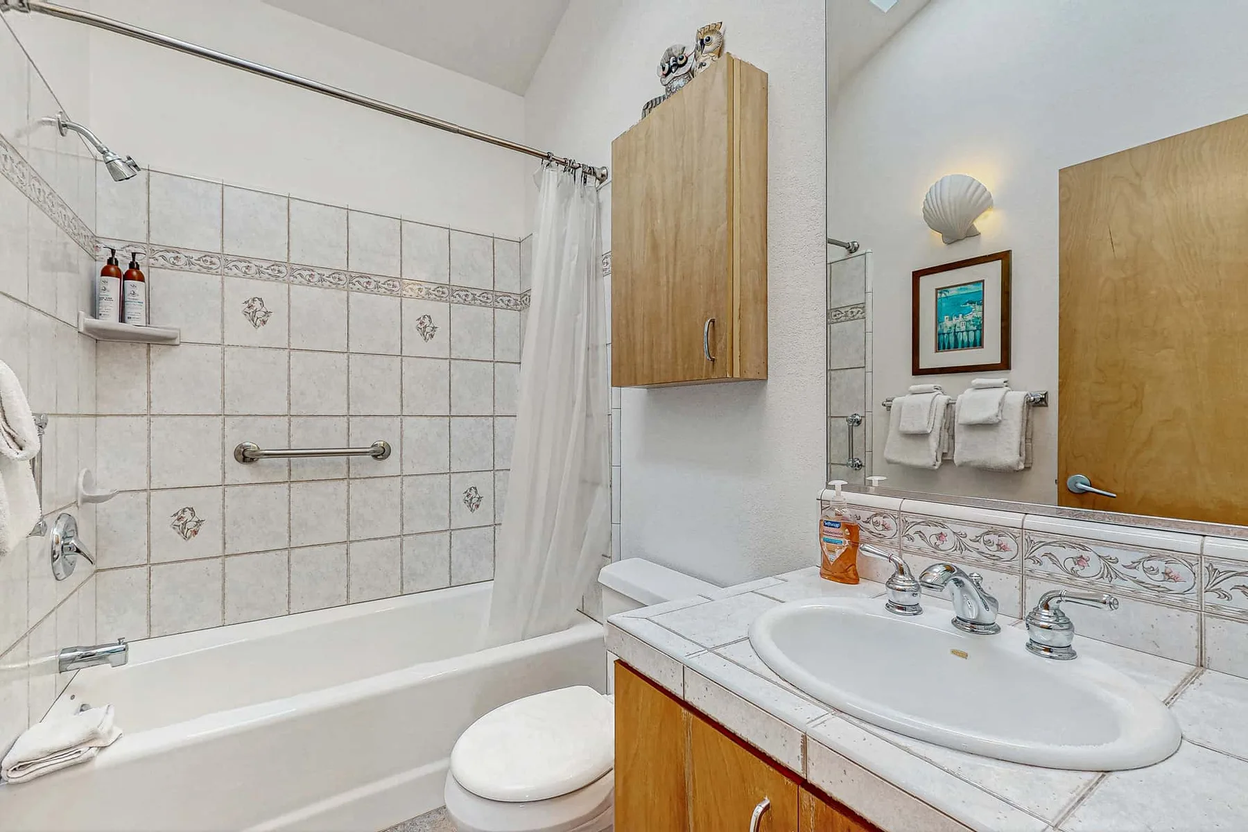 A tiled bathroom has a bathtub, toilet, and sink beneath a wall mirror.