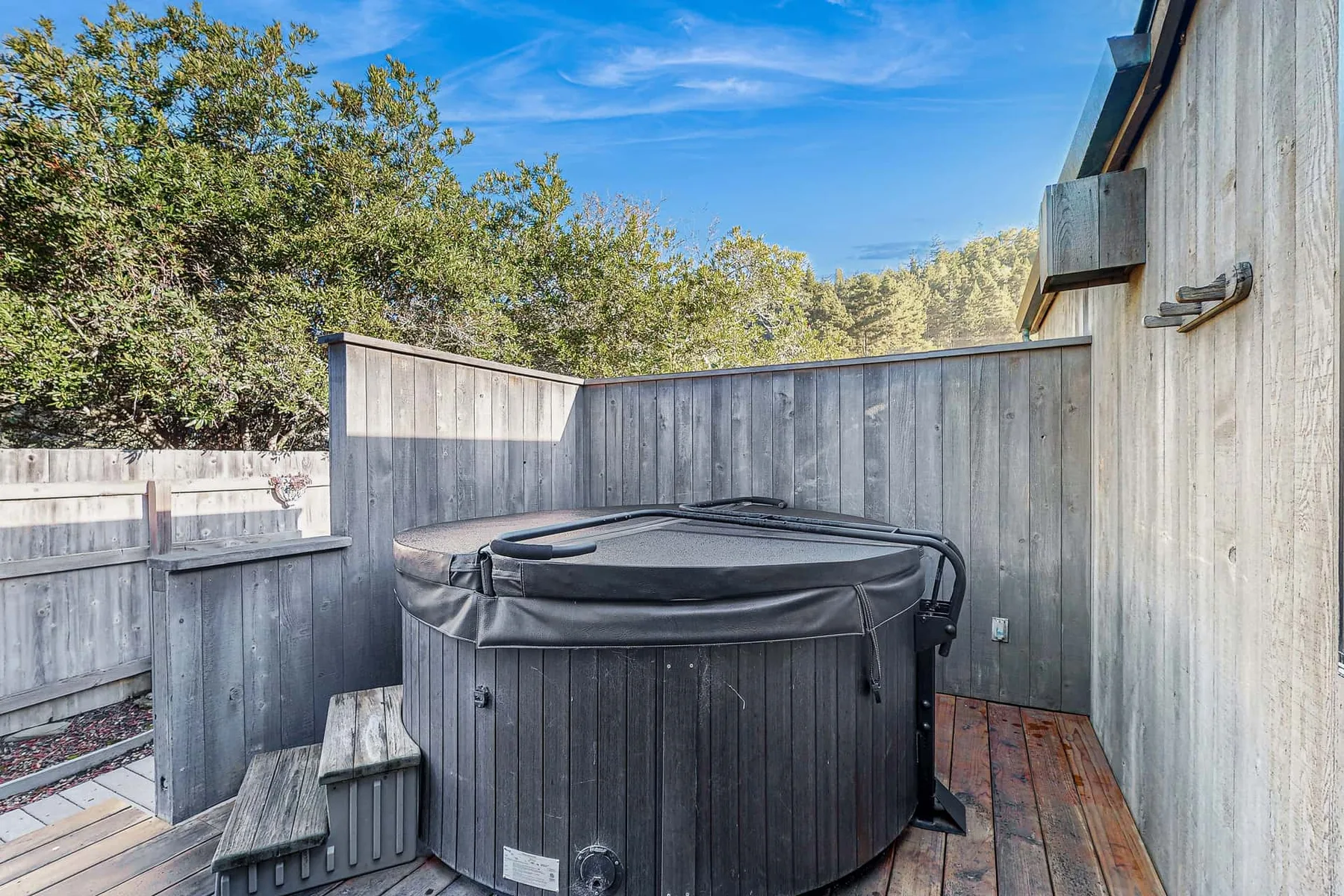 An outdoor hot tub sits on a wooden deck enclosed by tall fences.