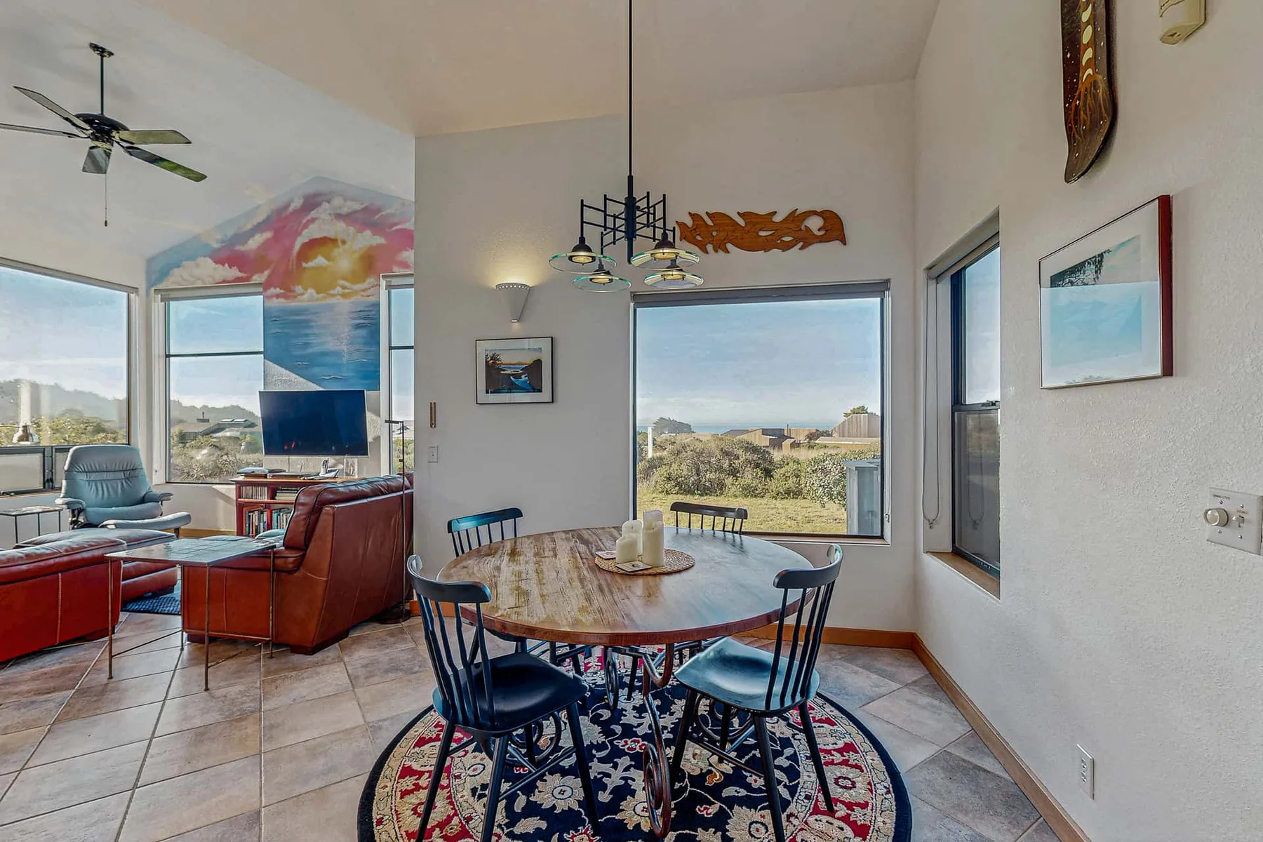 A bright dining and living area features a round table beside large windows.