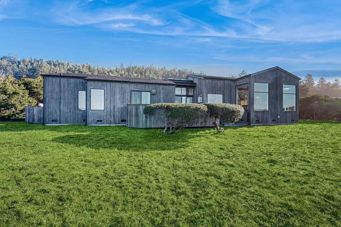 A modern house stands beside a broad green lawn under a blue sky.