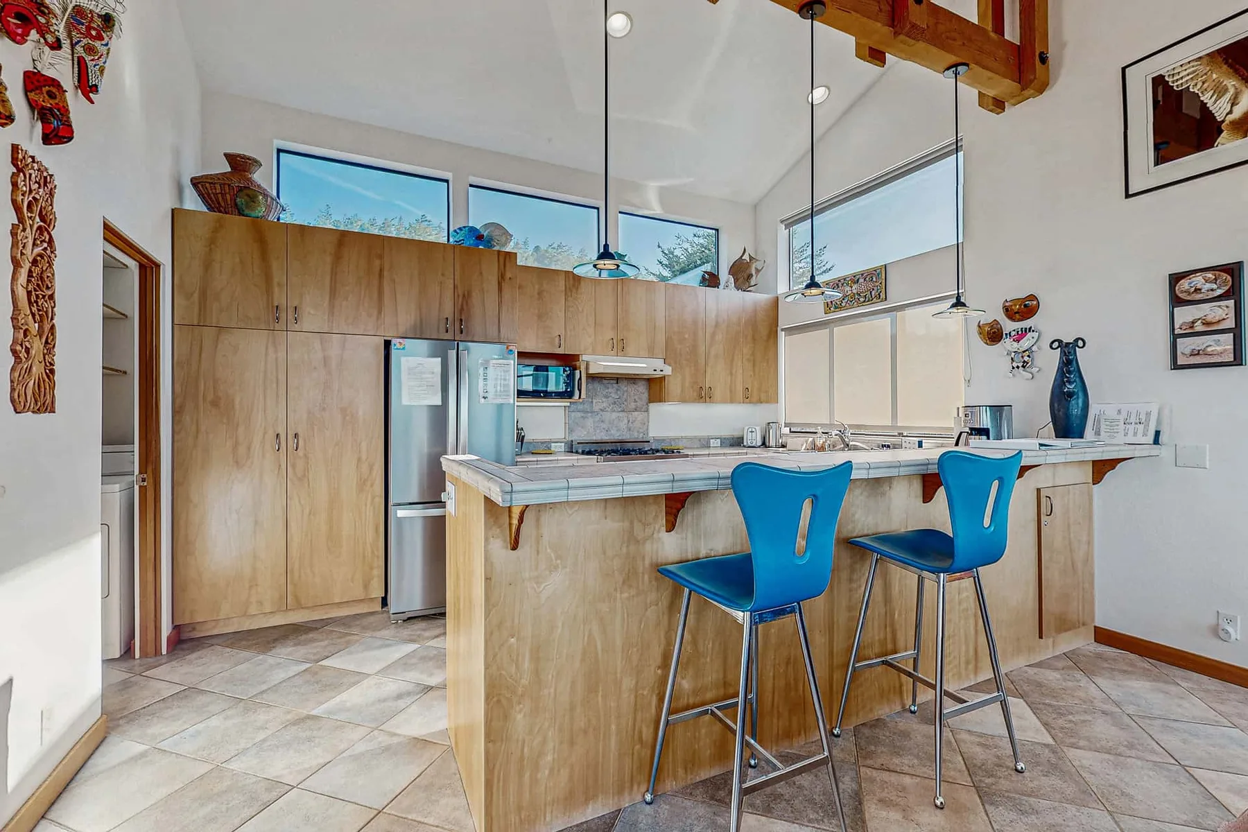 A bright kitchen with wood cabinets, a central island, and blue bar seating.
