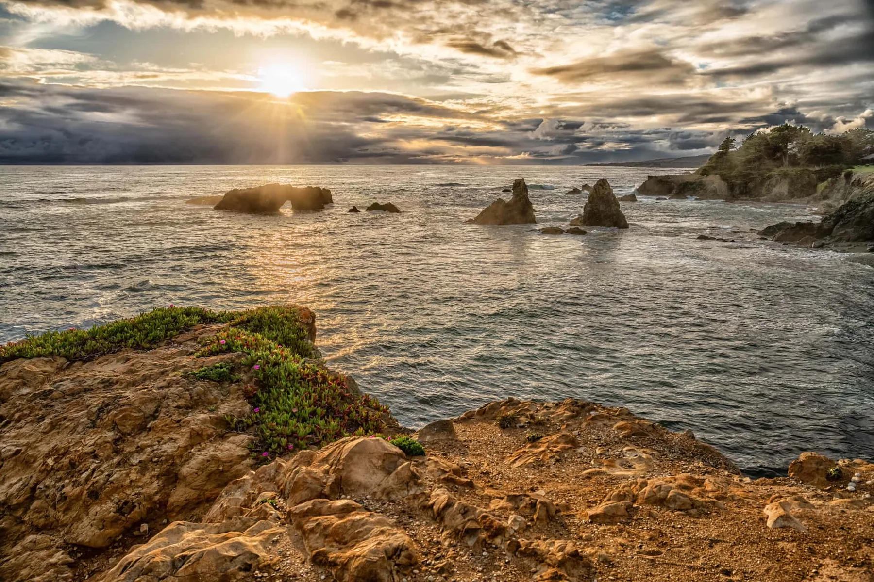 A rocky coastline overlooks the ocean beneath a cloudy sunset sky.