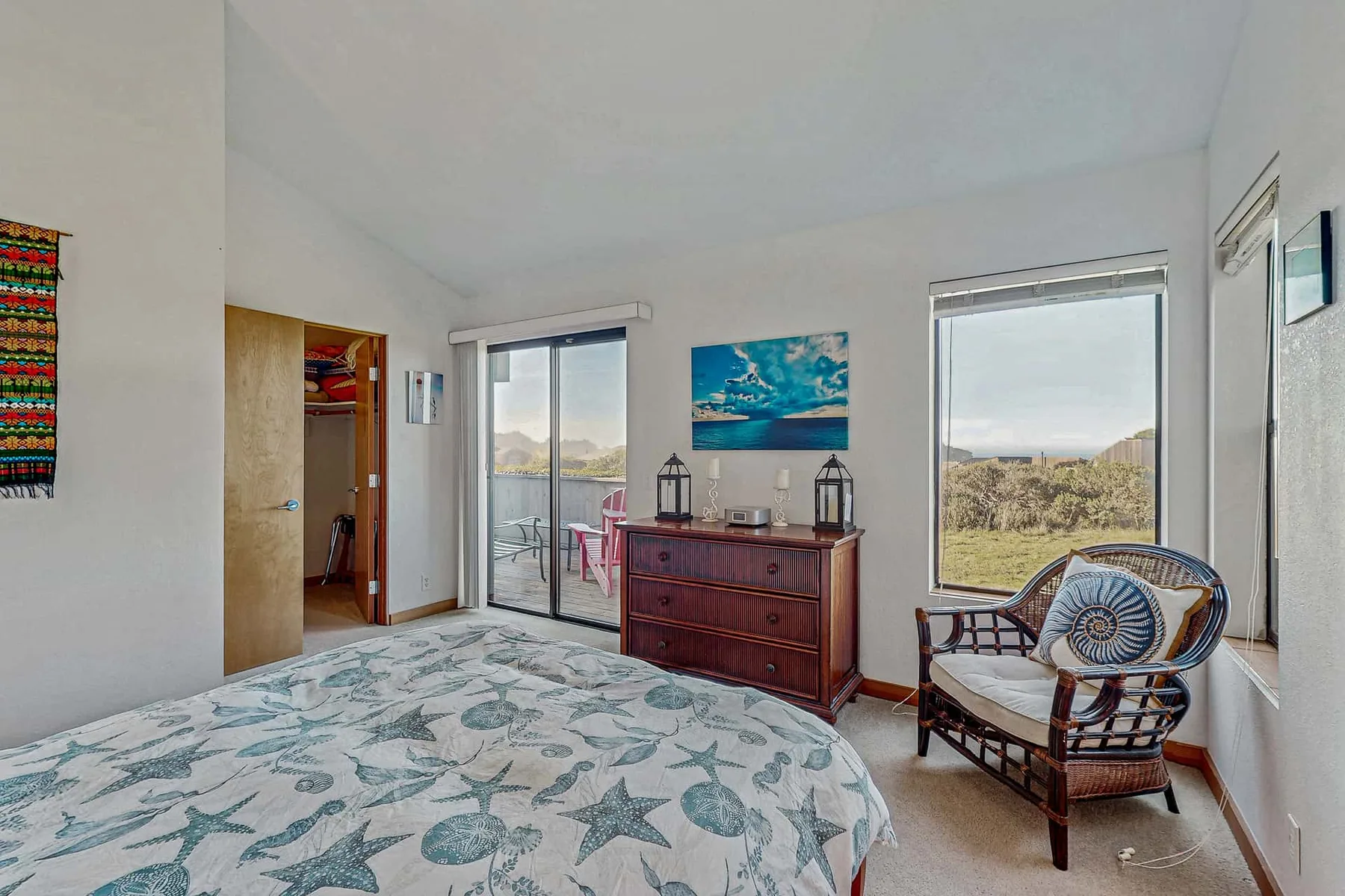 A bedroom with a patterned bedspread, wooden dresser, and seating by the window.