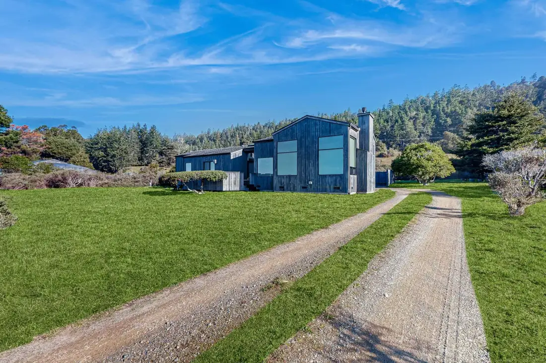 A modern house stands beyond a gravel driveway, with a broad green lawn.