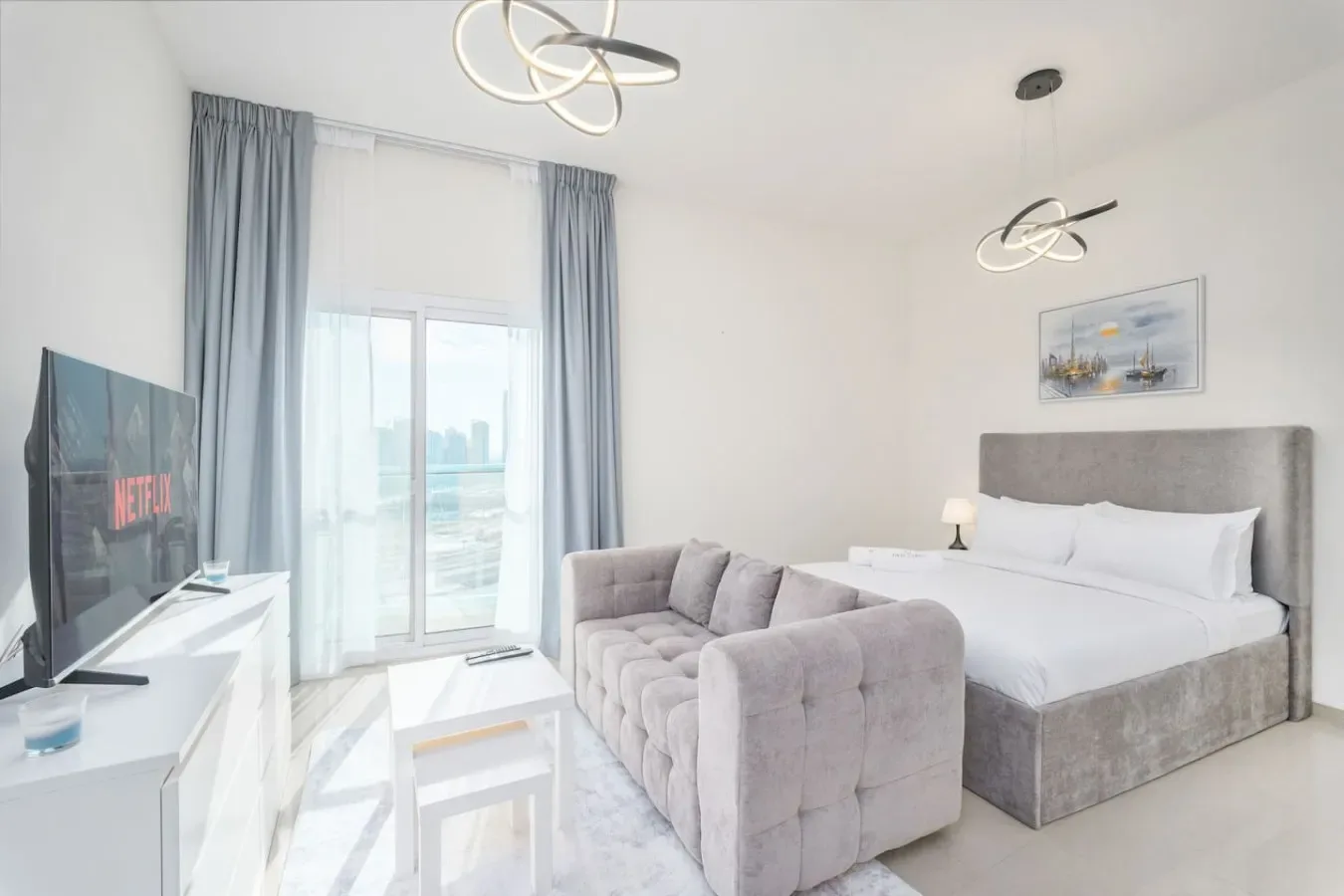 A bright bedroom with a bed, upholstered seating, and a glass balcony door.