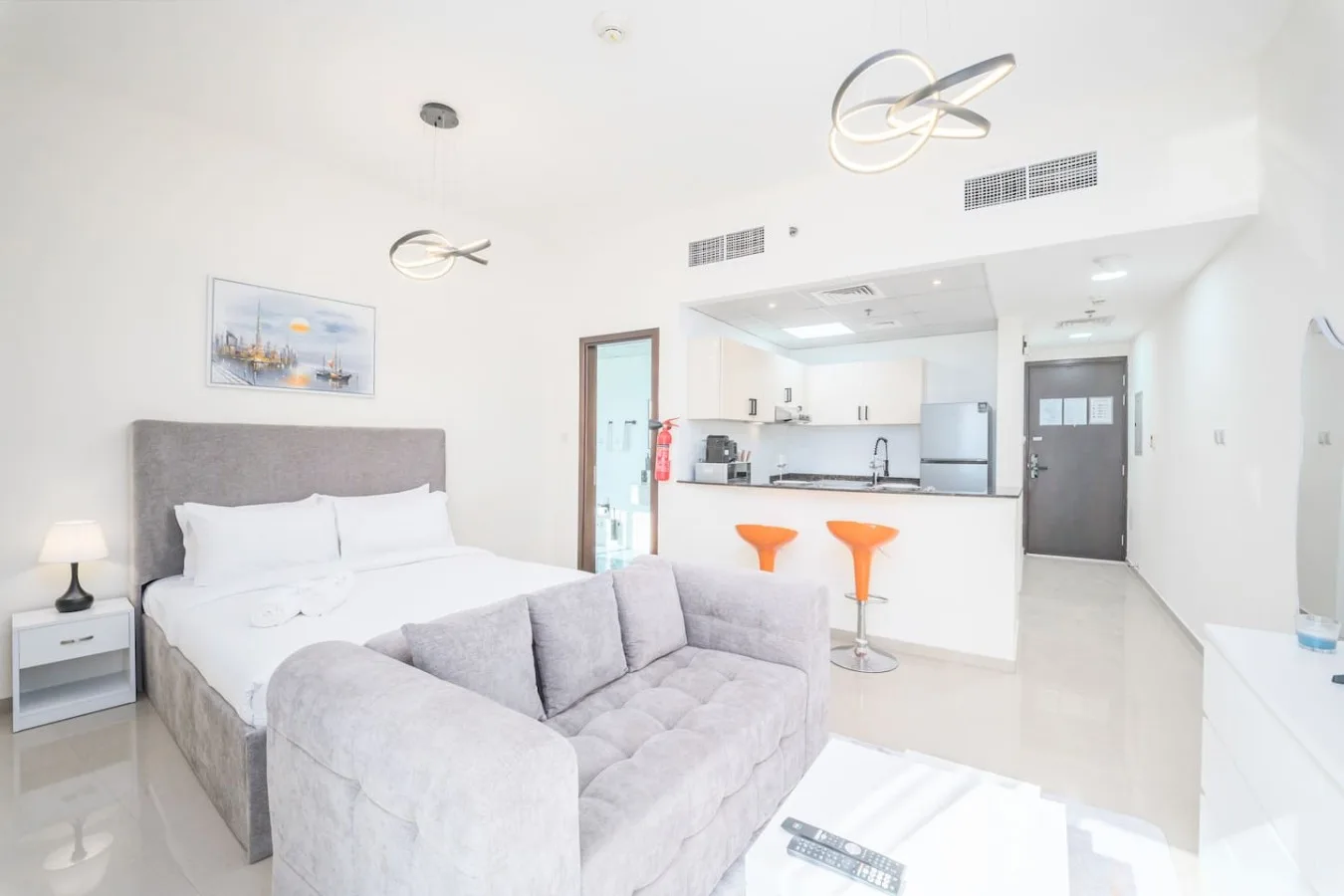 A bright studio room with a bed, sofa, and open kitchen area.