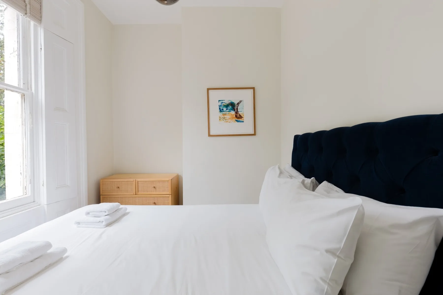 A bright bedroom with a white bed beside a large window.
