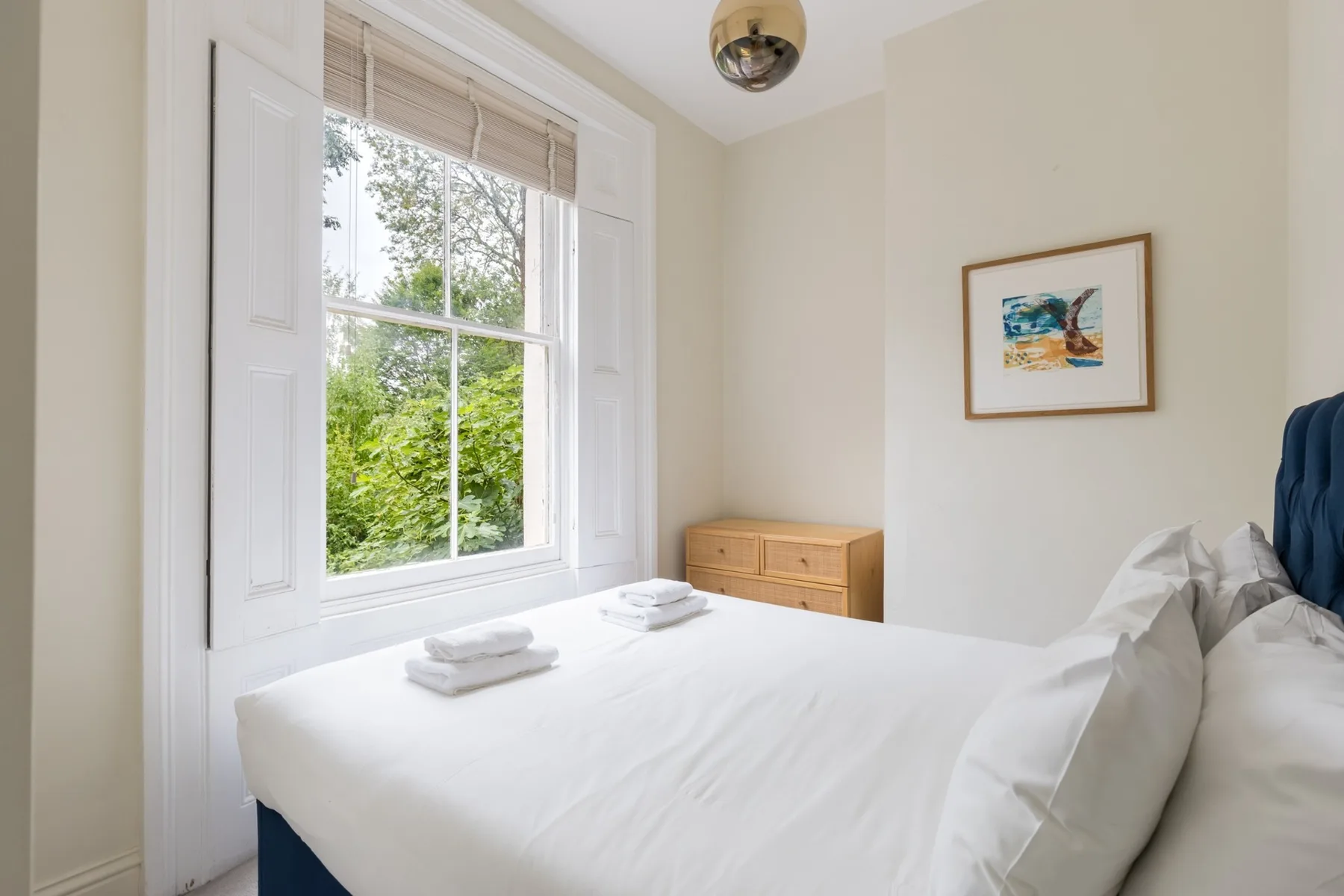 A bright bedroom with a neatly made bed beside a large window.