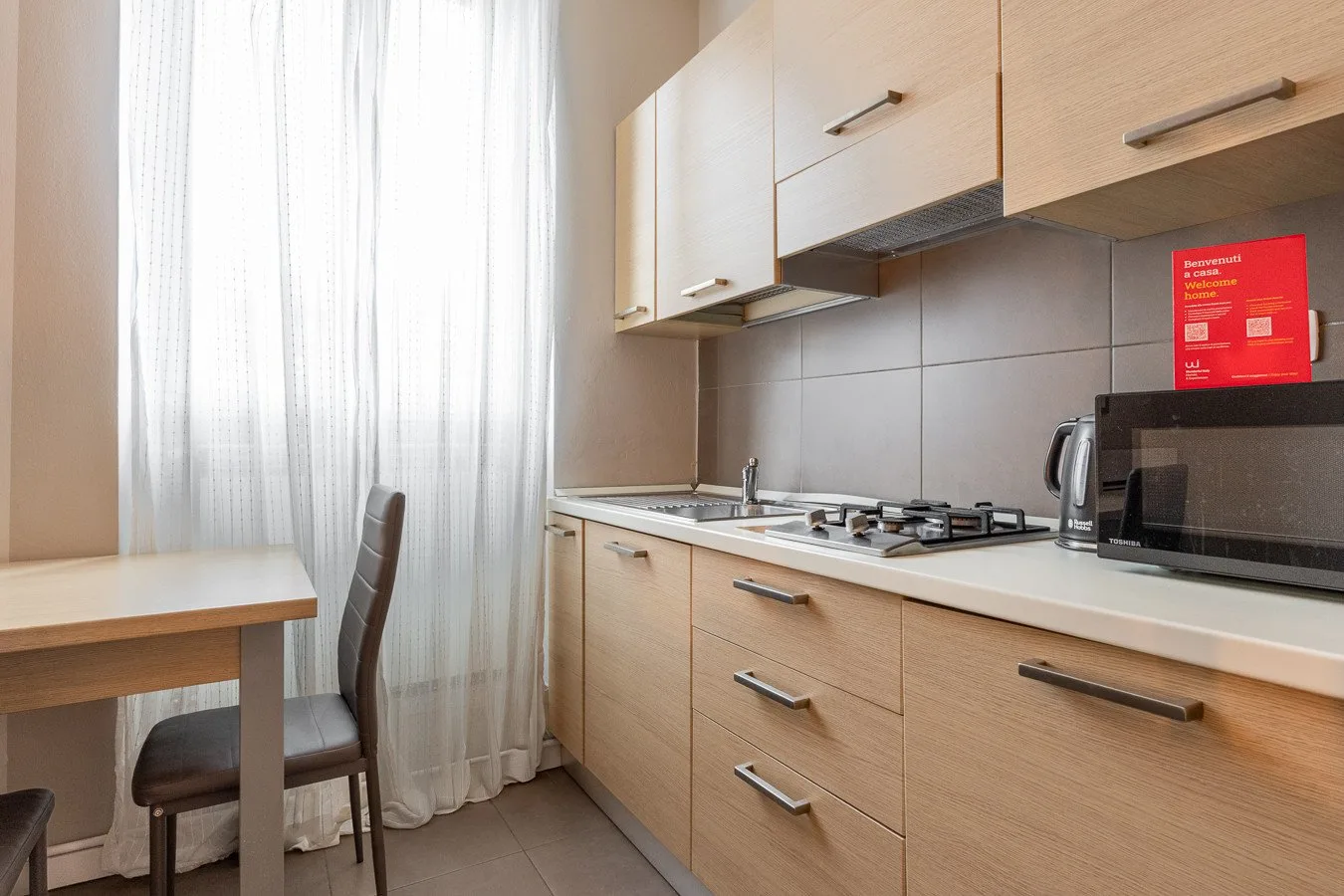 Una cocina compacta con gabinetes claros, una encimera y una pequeña mesa de comedor.