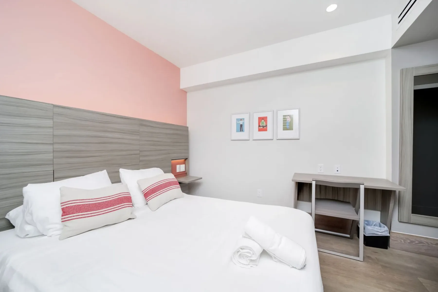 Petite bedroom with a bed, pillows, and wall art in a pink and gray color scheme.