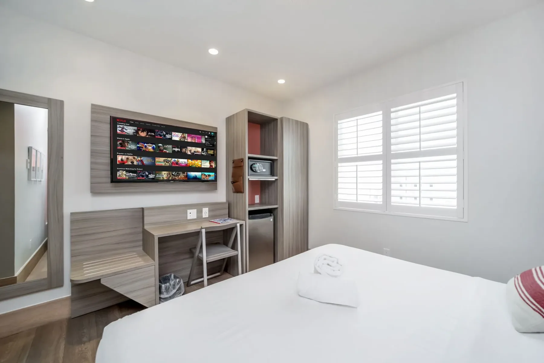 Hotel room with a bed, TV, desk, and shuttered window.