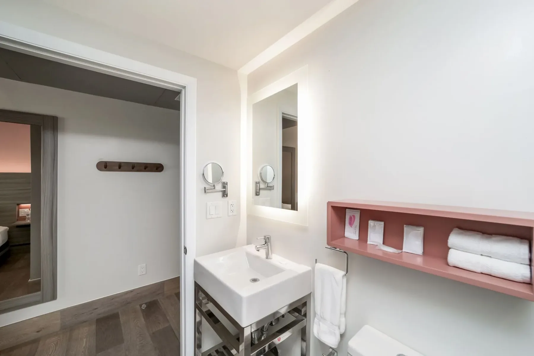 Bathroom with a white sink, mirror, and pink shelving; a bedroom doorway is visible.
