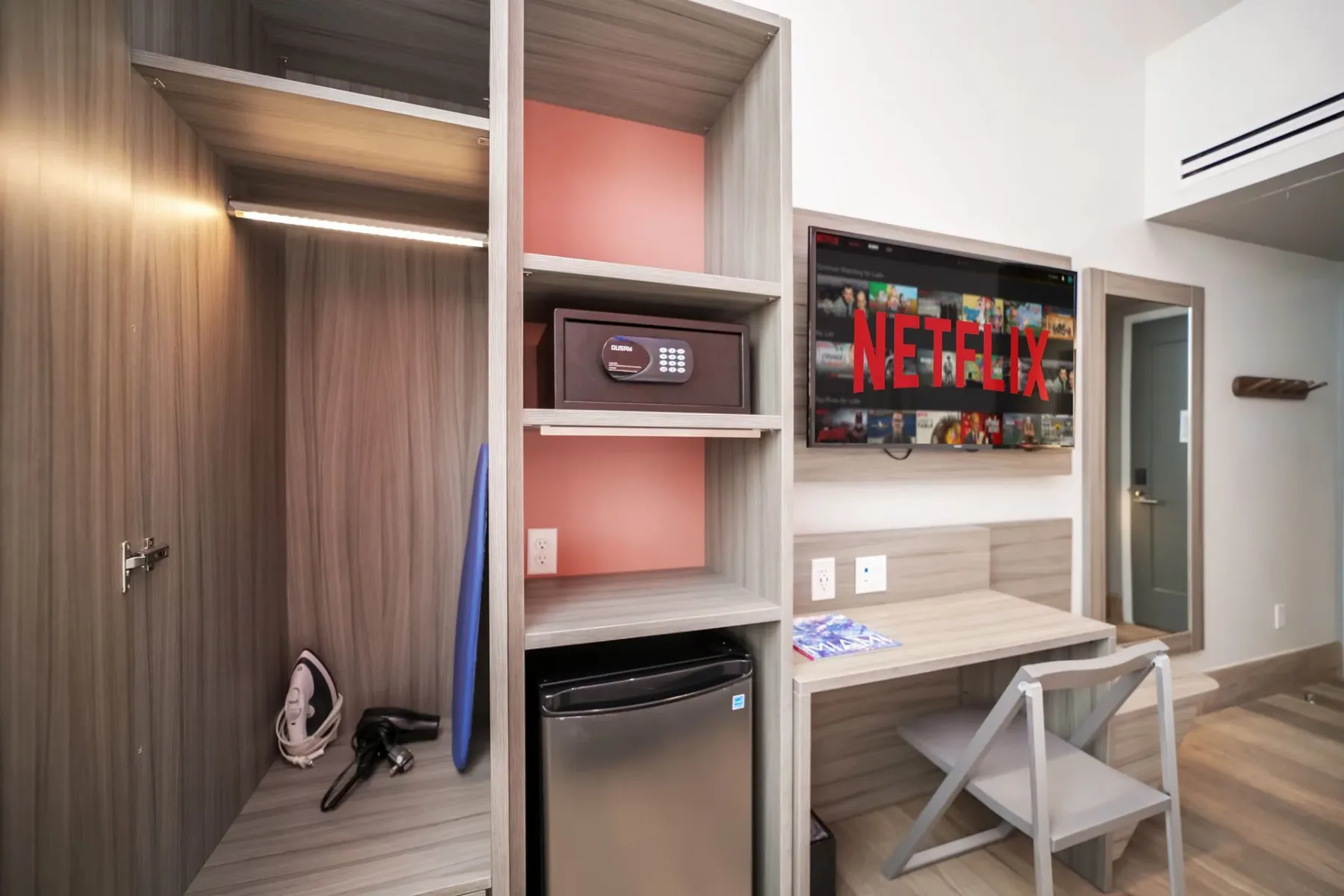 Hotel room with a closet, safe, desk, mini-fridge, and TV.