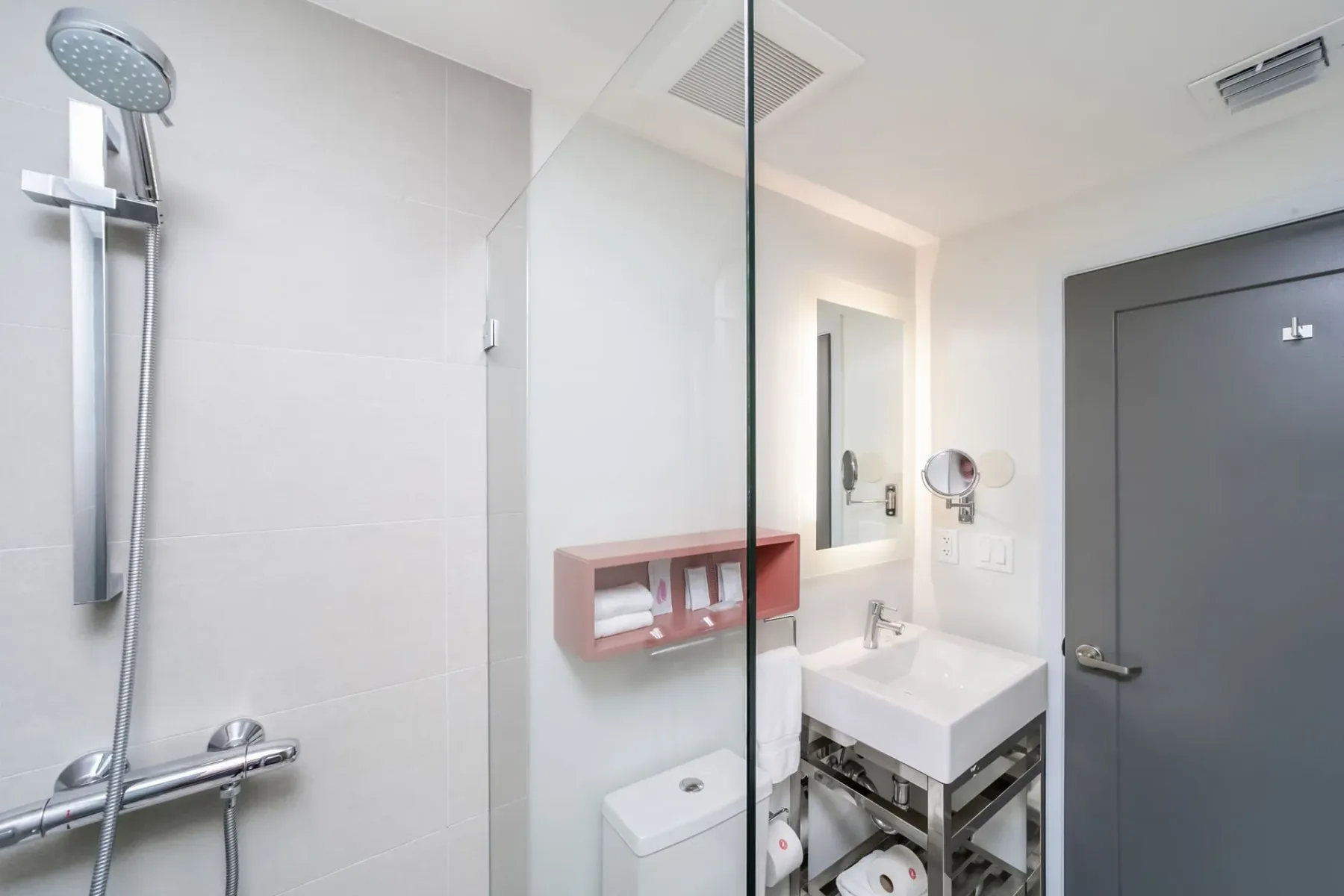 Bathroom with a shower, toilet, sink, mirror, and gray door.