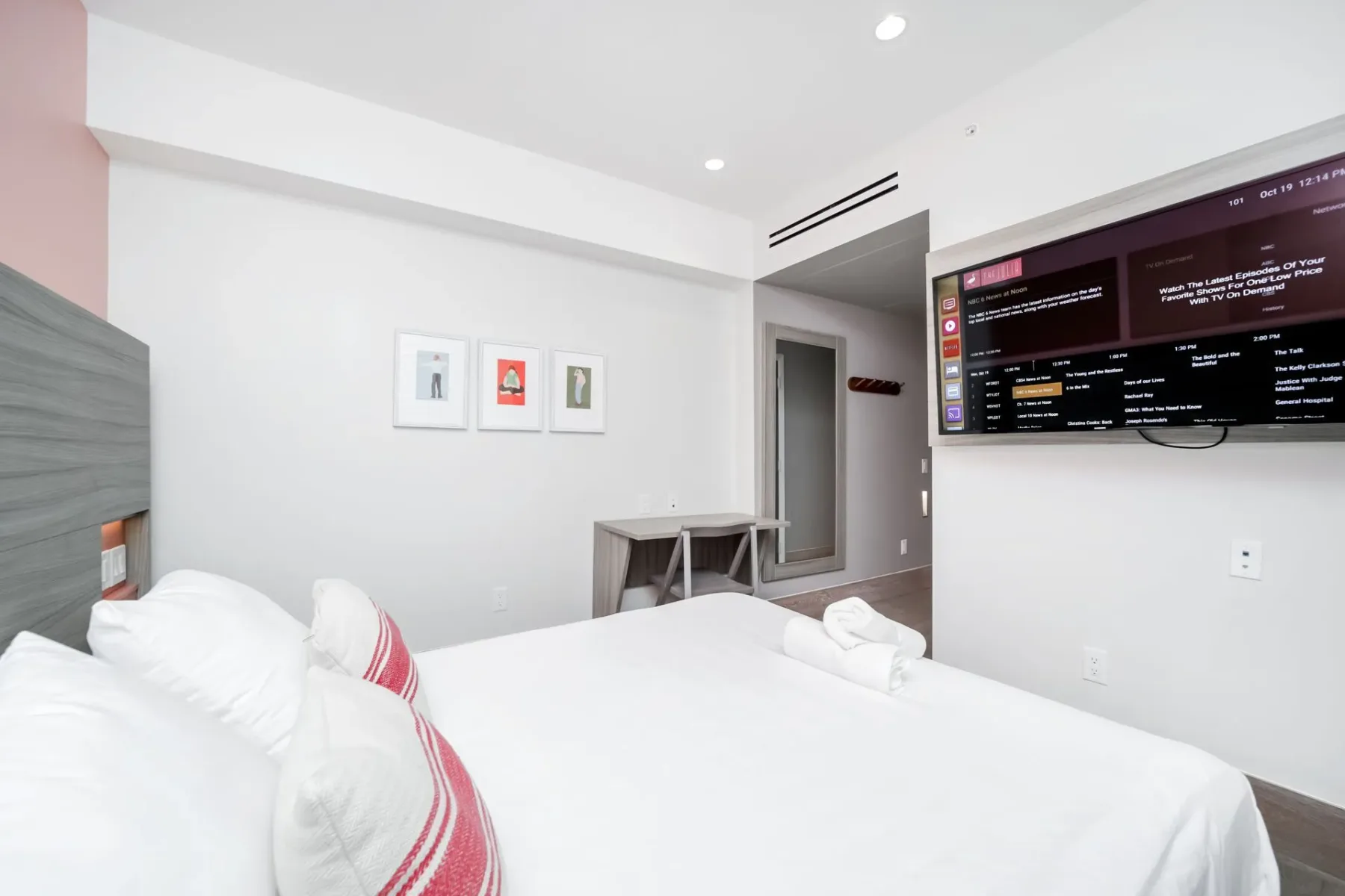 Petite bedroom with a white bed, wall-mounted TV, and small desk.
