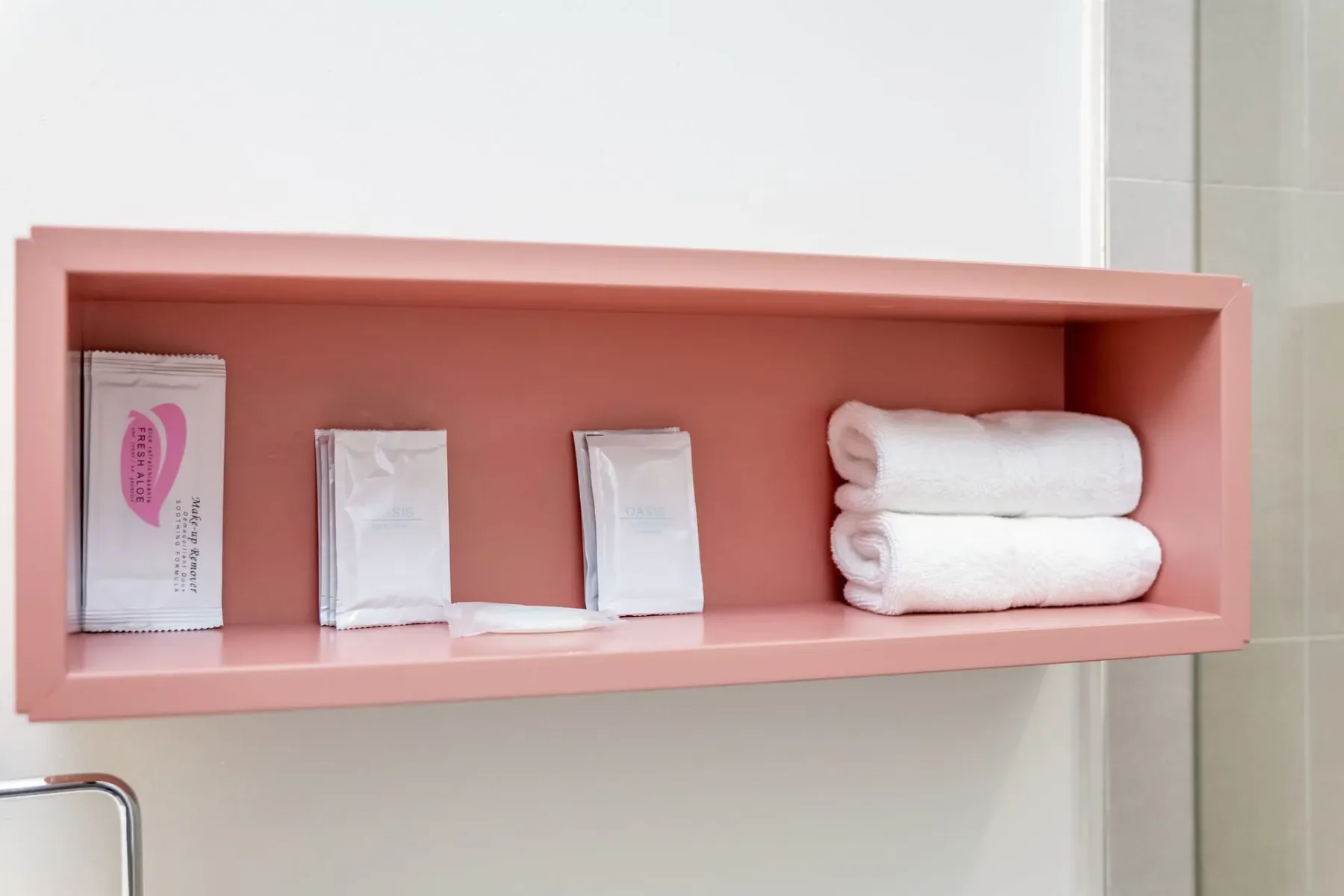Pink recessed bathroom shelf with toiletries and folded towels.