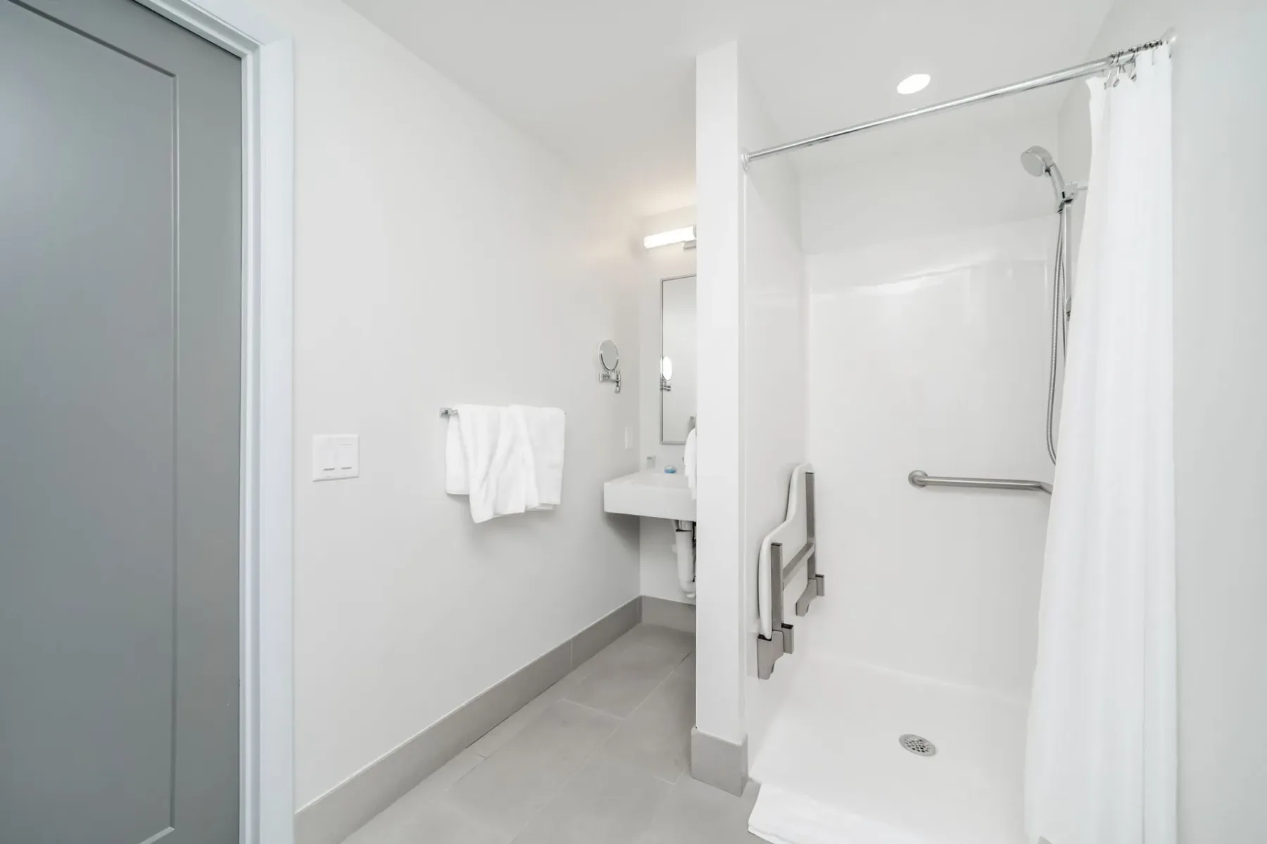 Petite bathroom with an open shower, grab bars, and sink.