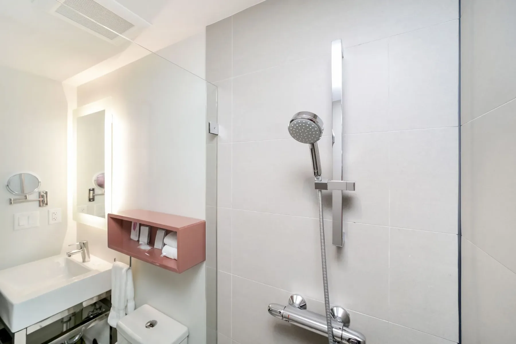Modern bathroom with a shower, sink, mirror, and pink shelf.