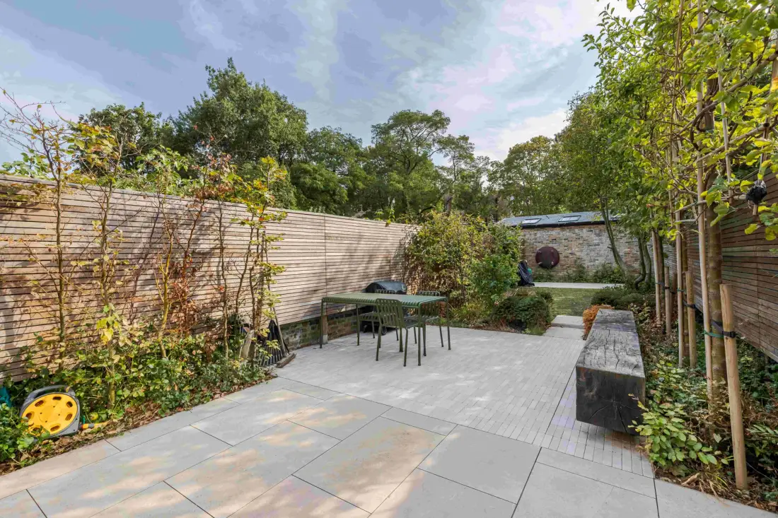 An outdoor patio with paved flooring, seating, and surrounding greenery.