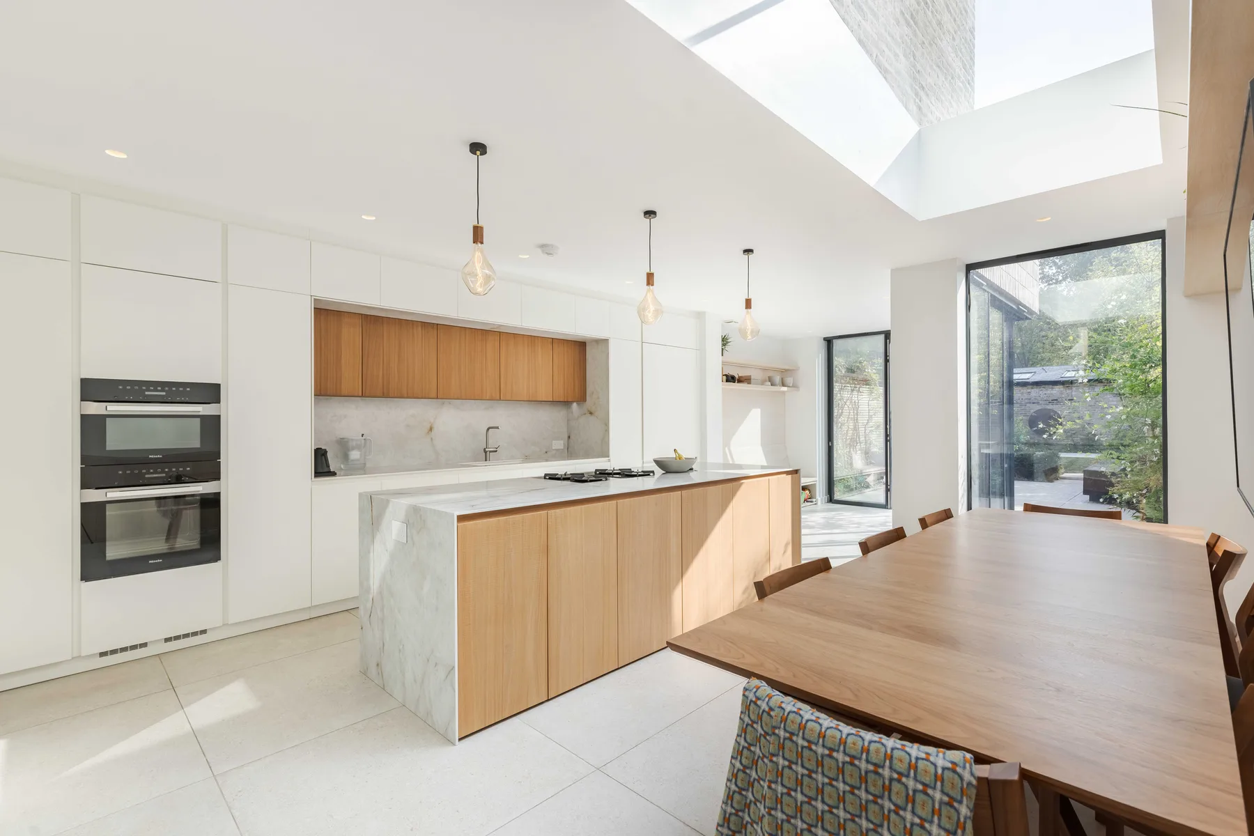 Una luminosa cocina moderna con comedor, mesa larga de madera e isla.