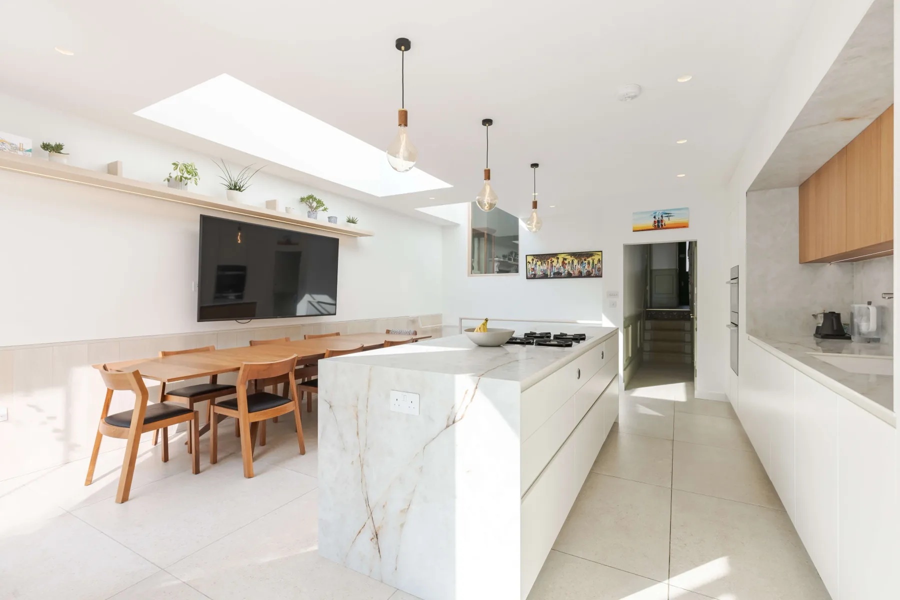 Cocina moderna y luminosa con una isla central, mesa de comedor y lámparas colgantes.