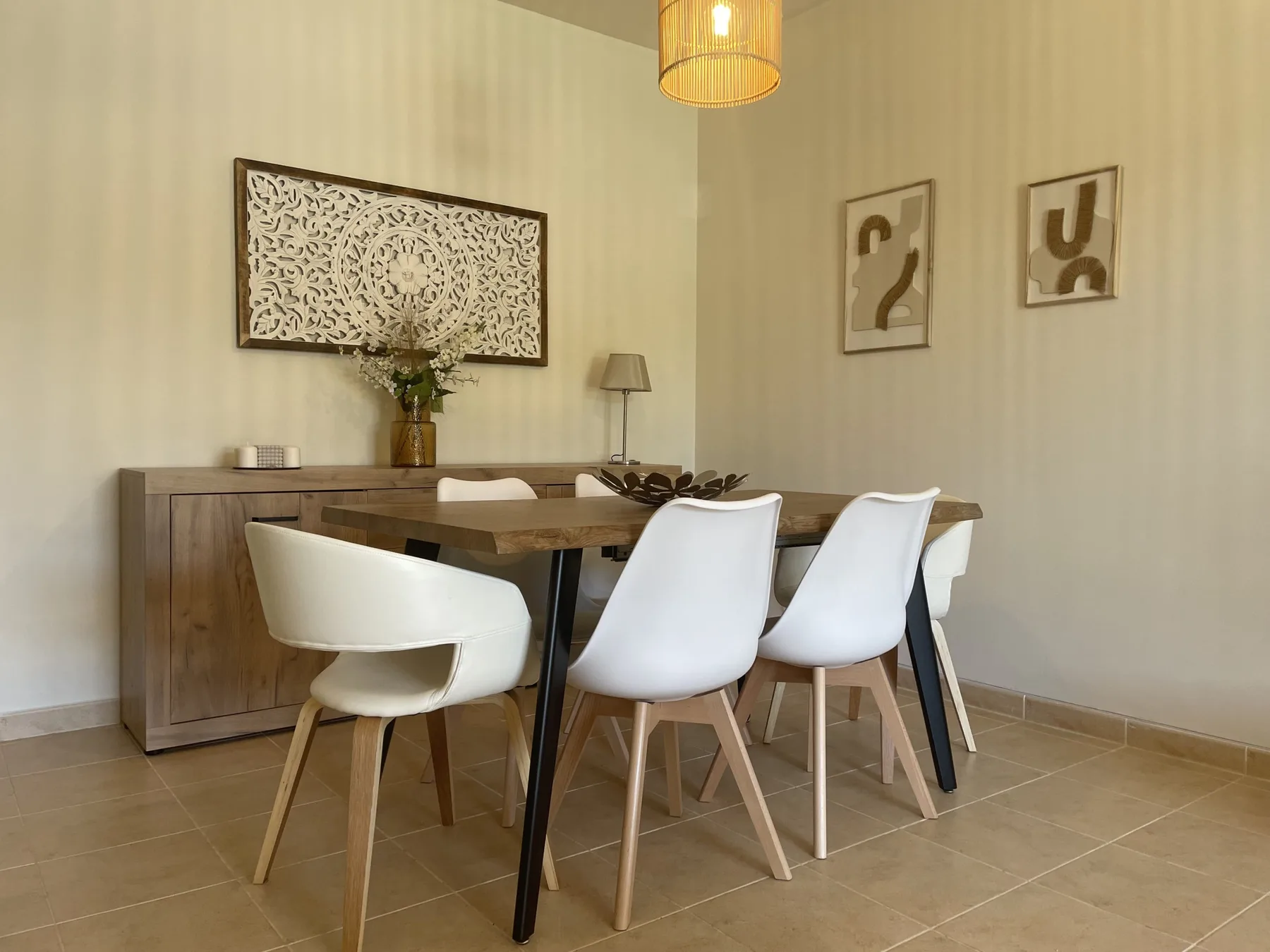 A dining area with a wooden table, white seating, and framed wall art.