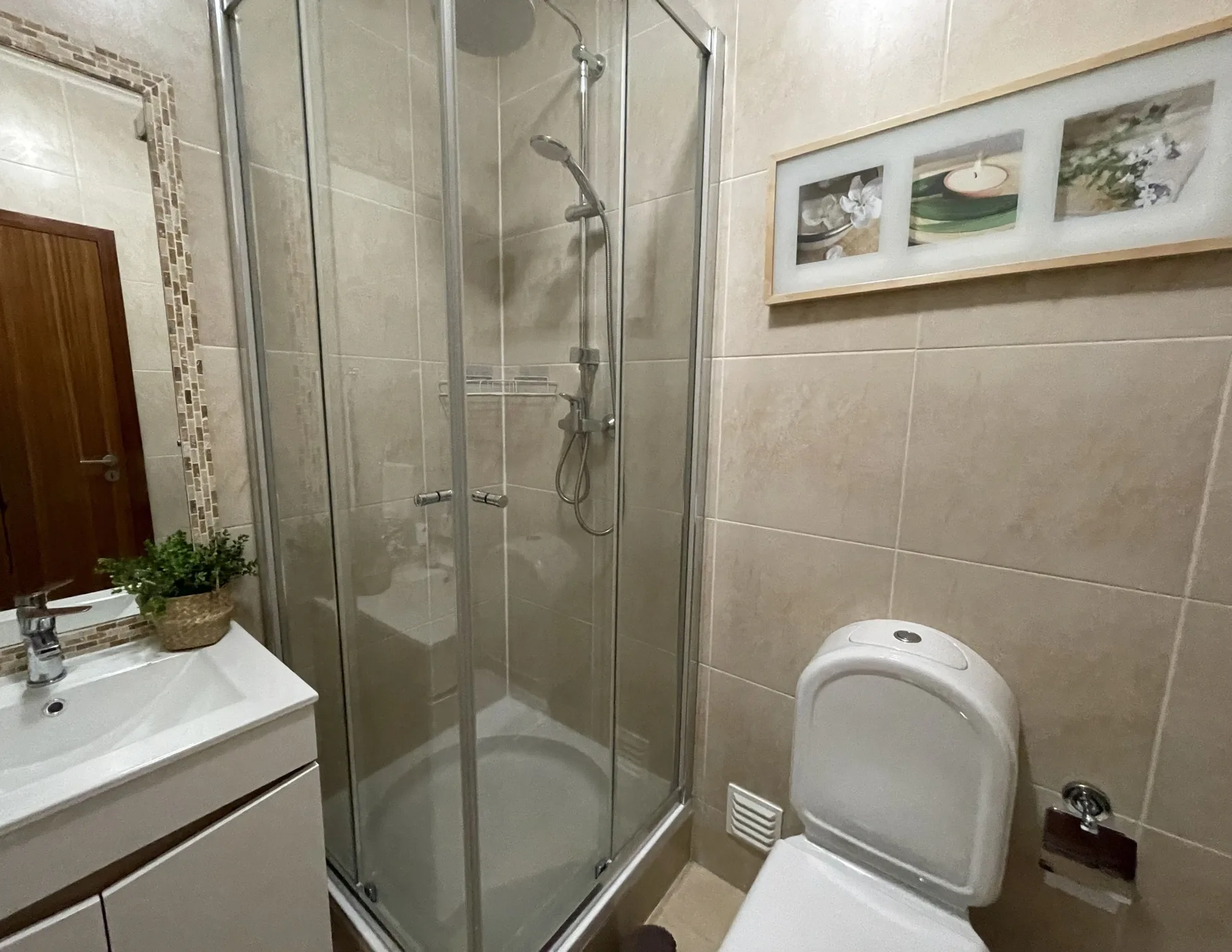 A tiled bathroom with a glass shower, sink, and toilet.
