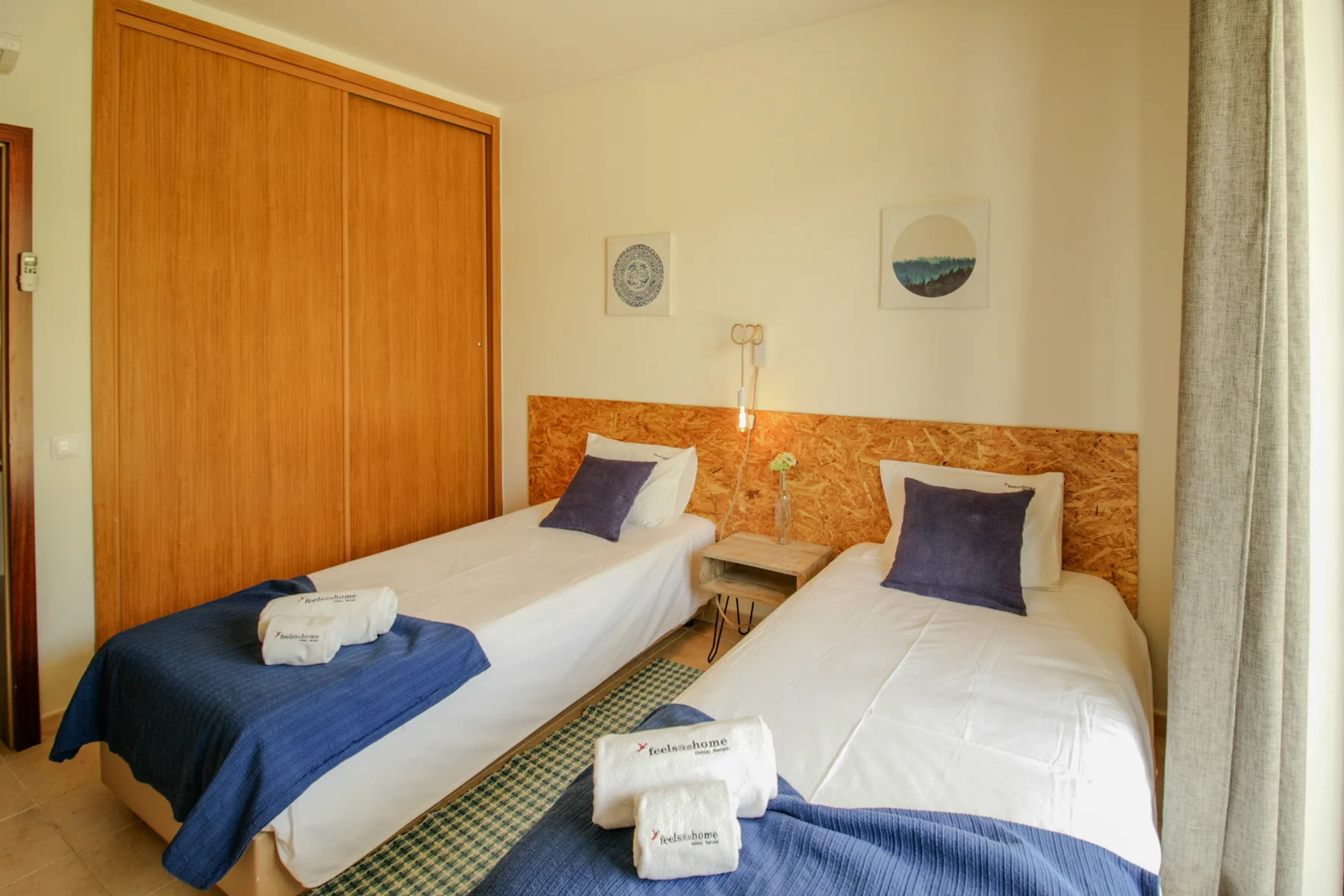 A twin bedroom with two beds, a wooden wardrobe, and a bedside table.