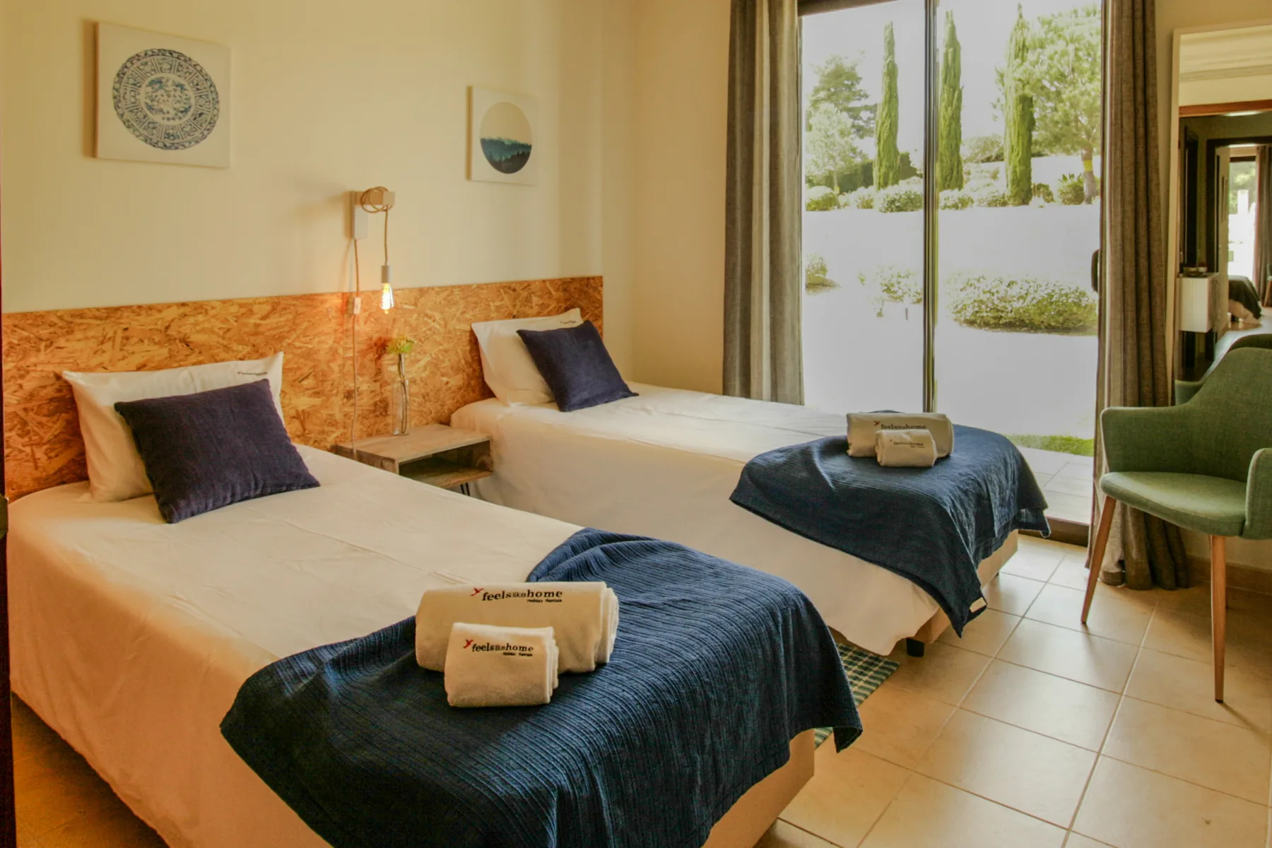 A bedroom with two beds, dark blue bedding, and a large window.