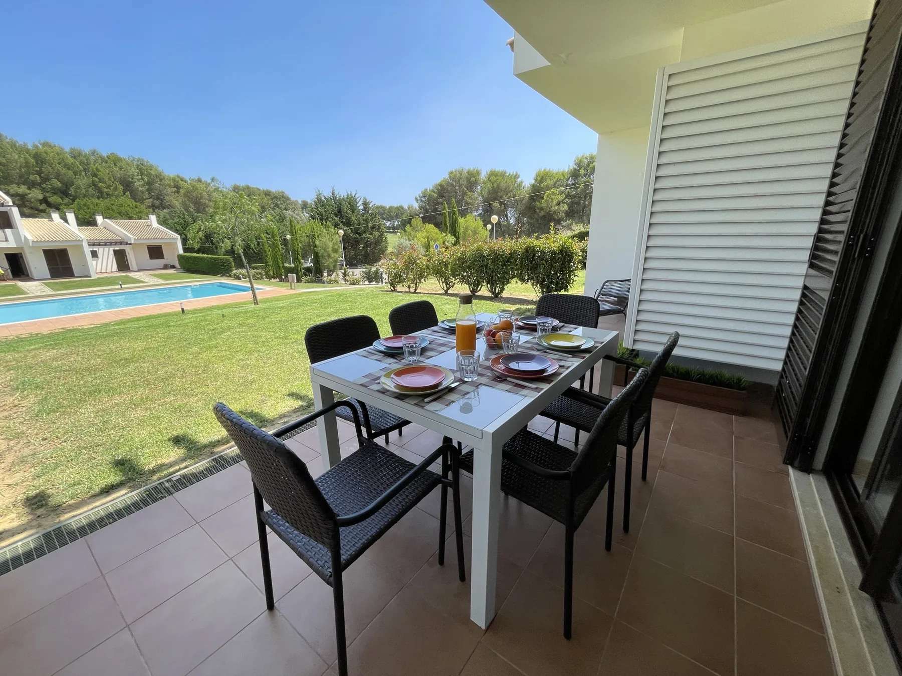 A furnished outdoor dining terrace overlooks a lawn and swimming pool.