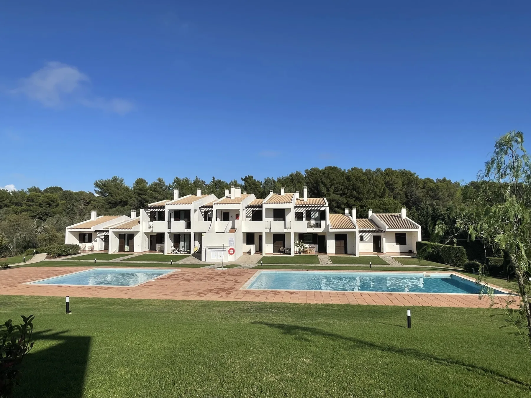 A row of white buildings faces a swimming pool and lawn.