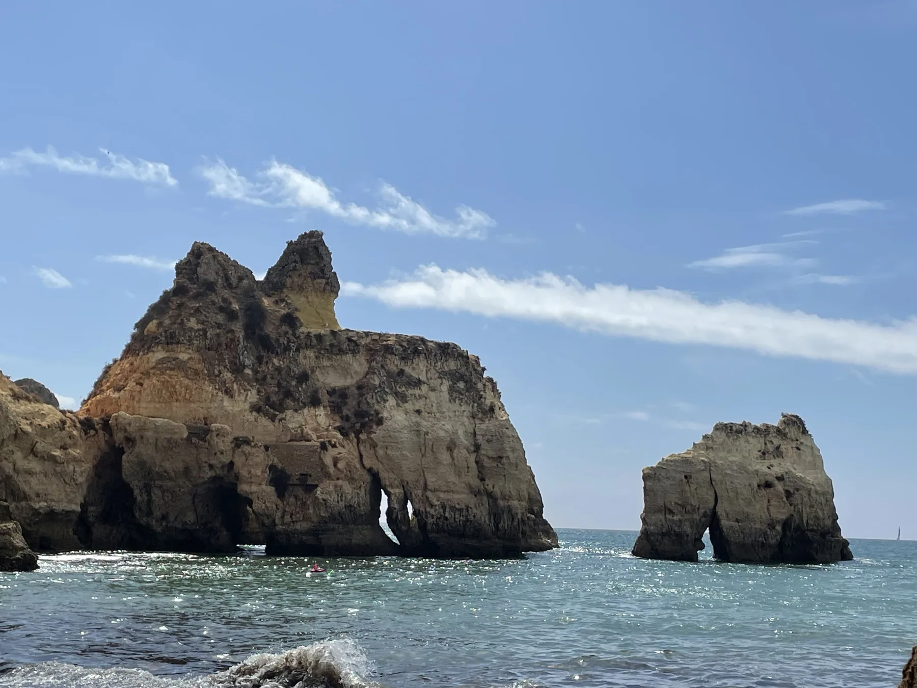 Rock formations rise from the sea beneath a clear blue sky.