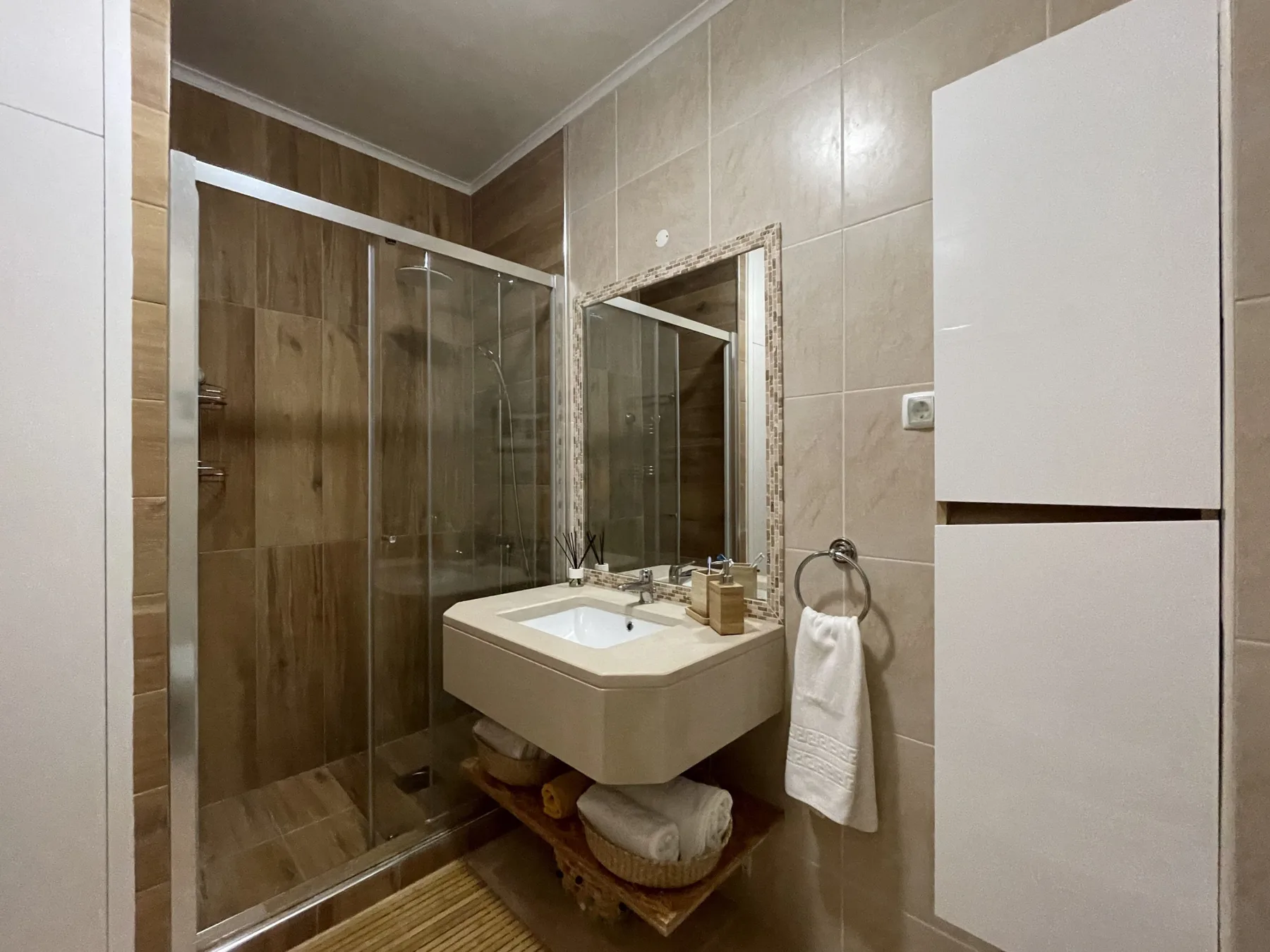 A tiled bathroom with a sink, mirror, and glass shower enclosure.
