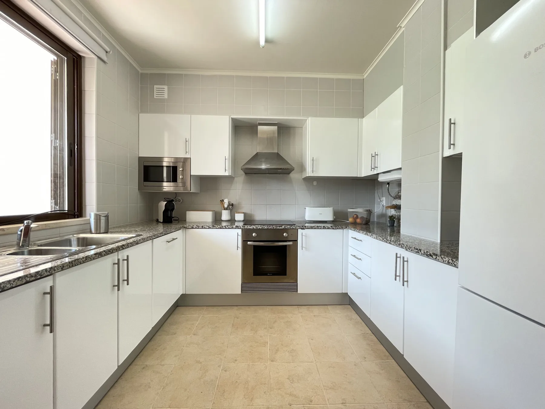 A bright kitchen with white cabinets, countertops, and built-in appliances.