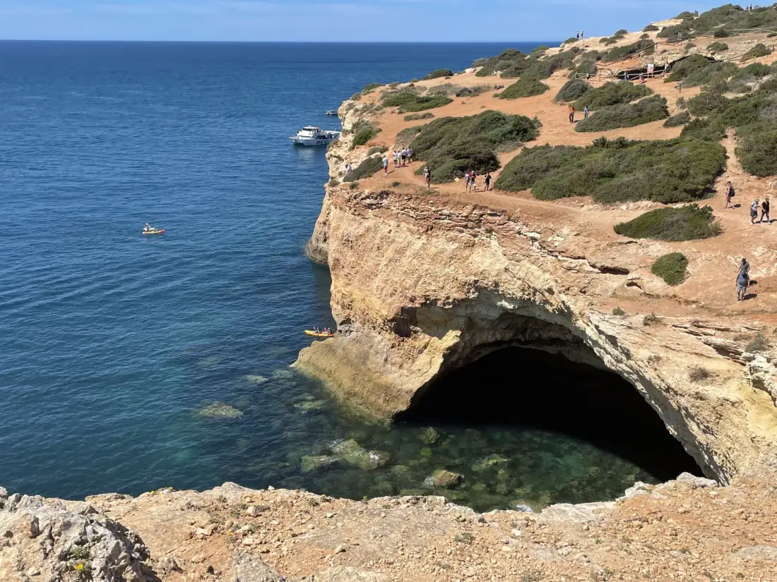 A coastal cliff with a large sea cave beside the blue ocean.